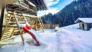 A wooden cabin with a red slide in the snow, surrounded by a forest.