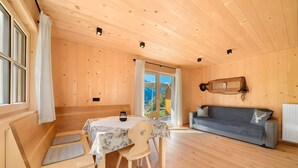 A wooden interior with a dining table, chairs, a sofa, and a window with curtains. - Apartment 'Jaufenspitz' with Mountain View, Private Panoramic Terrace and Wi-Fi (Sankt Martin in Passeier)