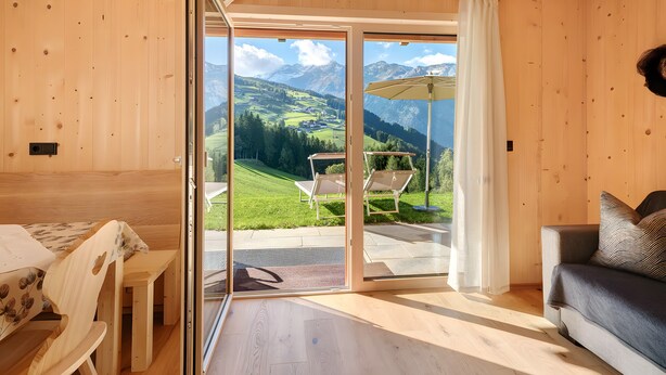 A wooden interior with a sliding glass door to a balcony, a sofa, and a table with chairs. - Apartment 'Jaufenspitz' with Mountain View, Private Panoramic Terrace and Wi-Fi (Sankt Martin in Passeier)