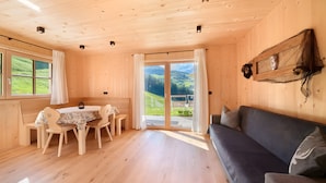 A wooden interior with a dining table, chairs, a sofa, and a large window offering a view of greenery. - Apartment 'Jaufenspitz' with Mountain View, Private Panoramic Terrace and Wi-Fi (Sankt Martin in Passeier)