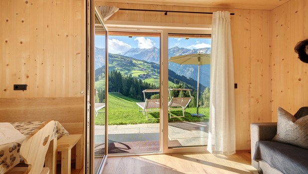 Ein Holzinnenraum mit einer Schiebetür aus Glas, die zu einem Außenbereich mit Bergblick führt.