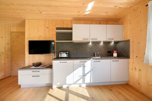 Cocina compacta con paredes de madera, un televisor de pantalla plana, armarios blancos y una encimera con un tostador.