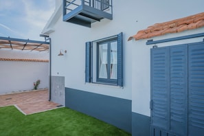 Et moderne hus med balkon, vindue med stormskærm og fliseterrasse.