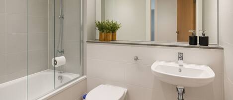 A modern bathroom with a glass-enclosed shower, a white toilet, and a sink with a mirror above it.