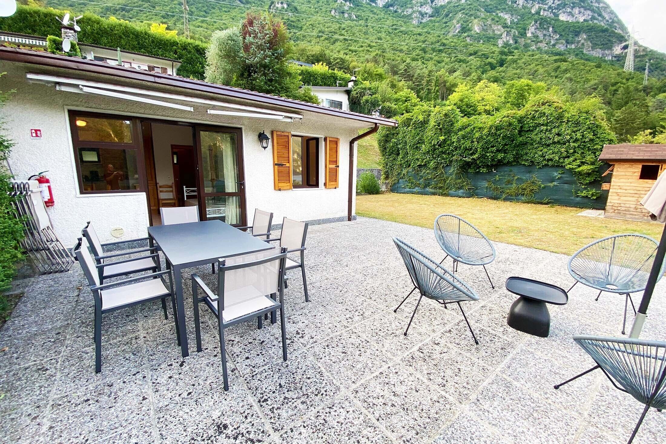 Un patio con mesa y sillas, un pequeño edificio de fachada blanca y montañas al fondo.