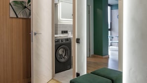 Un interior moderno con una puerta de madera, un banco tapizado en verde, una lavadora y vistas a una habitación con una pared verde y una ventana.