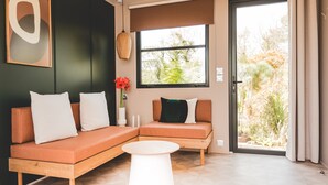Un salon moderne avec un canapé d’angle, une table basse ronde et une grande fenêtre donnant sur un paysage verdoyant.