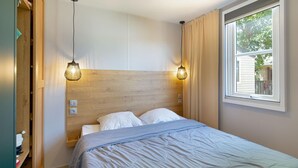 Une chambre à coucher avec une tête de lit en bois, deux lampes de chevet, une fenêtre avec des rideaux et un lit recouvert d’une couverture bleue.