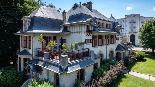 A large, historic building with multiple levels, a prominent balcony, and a well-maintained garden. - Germaine" guest room (Vittel)
