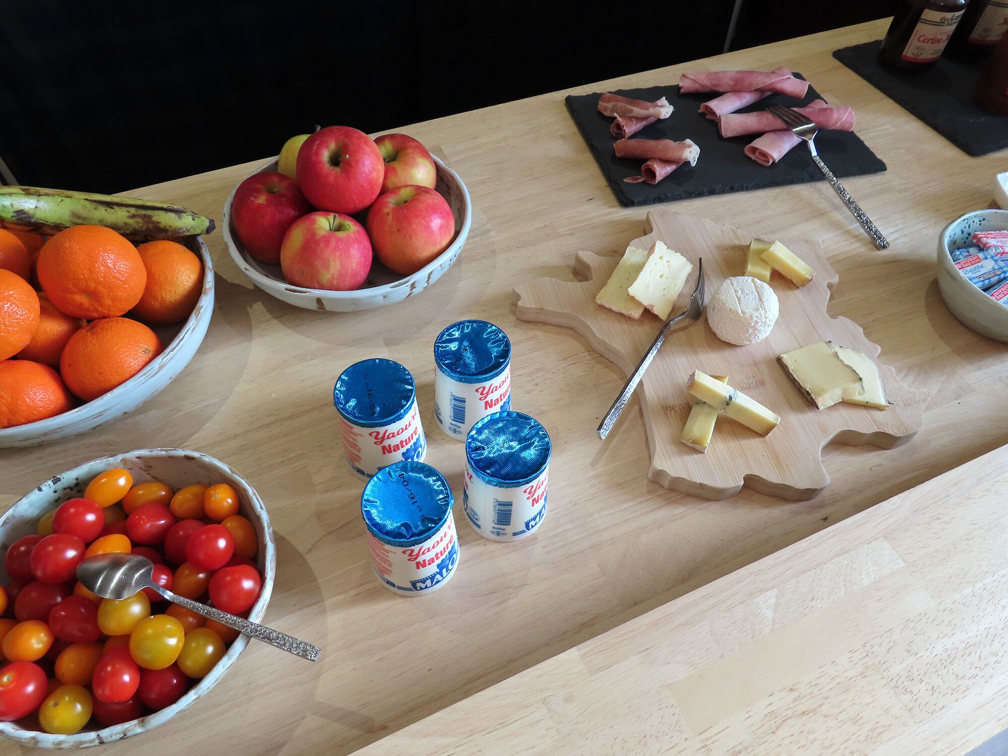 Una mesa con diferentes alimentos, entre ellos manzanas, naranjas, queso y bebidas en lata.