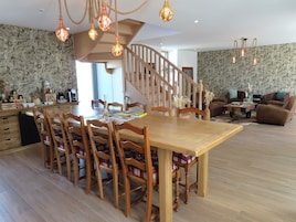 Uma área de refeições com mesa e cadeiras de madeira, uma escada e uma sala de estar com sofá e mesa de centro.