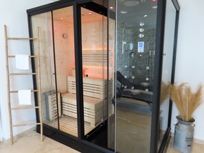 A sauna room with wooden benches, a glass door, and a metal heater. - Le Foyer Celtique (Ploërmel)