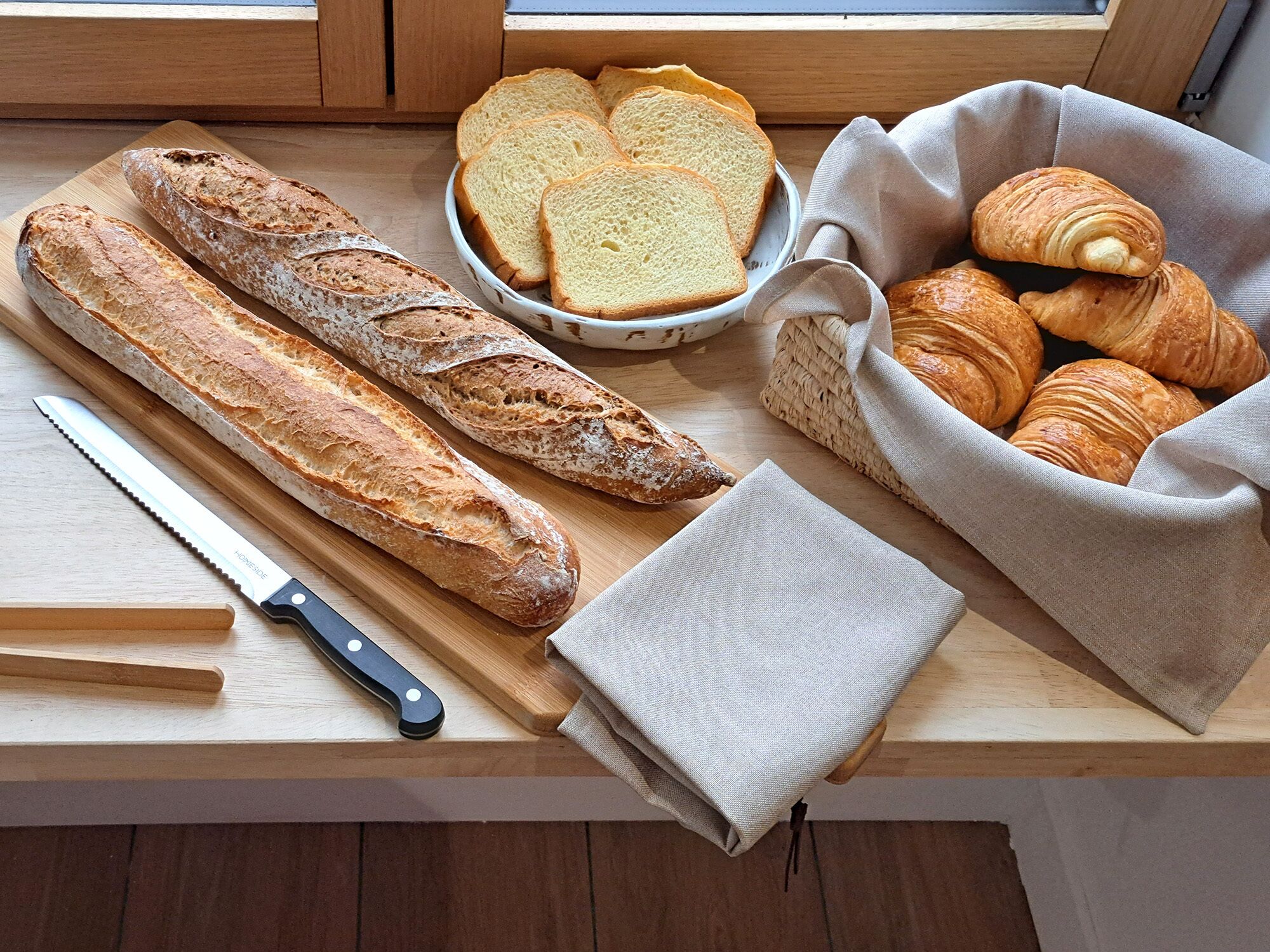 Un plan de travail de cuisine avec du pain, un couteau et un panier de croissants.