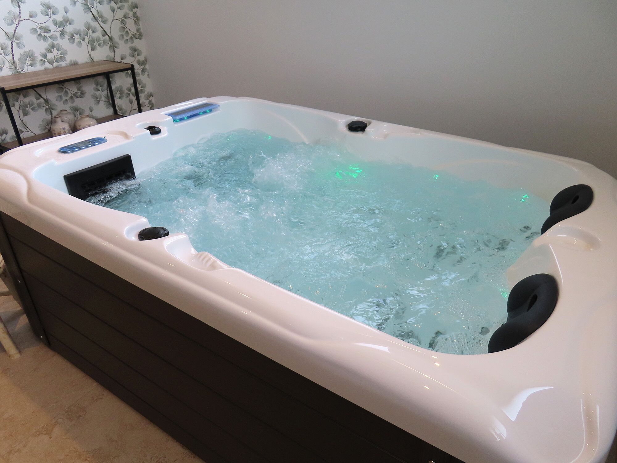 A hot tub with water jets, a control panel, and a wooden shelf.