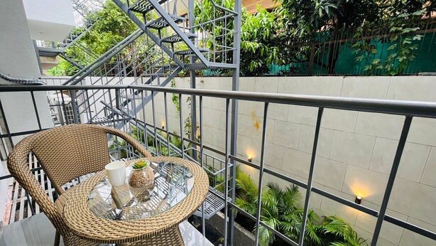 A balcony with a wicker chair, a glass table, and a small potted plant. - Stay near - Hotel near me Gurgaon (Gurugram)