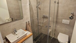 Uma casa de banho moderna com cabine de duche em vidro, uma sanita e uma pia branca.