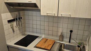 Uma cozinha compacta com armários brancos, uma pia de aço inoxidável e um fogão preto.