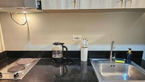A kitchen with a stove, a coffee maker, a sink, and a utensil holder. - Cozy 1-bedroom condo with WiFi, AC Near SM Mall of Asia (Pasay City)