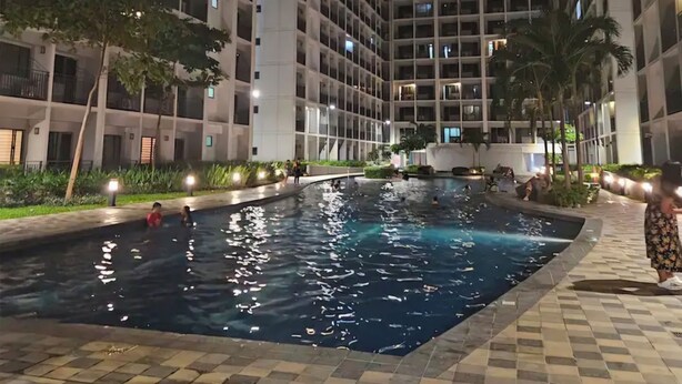 A nighttime view of a high-rise building with a swimming pool surrounded by greenery and a paved walkway. - Cozy 1-bedroom condo with WiFi, AC Near SM Mall of Asia (Pasay City)