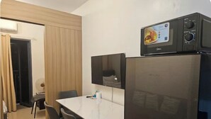 A compact kitchen with a refrigerator, a microwave, and a flat-screen TV mounted above the counter. - Cozy 1-bedroom condo with WiFi, AC Near SM Mall of Asia (Pasay City)