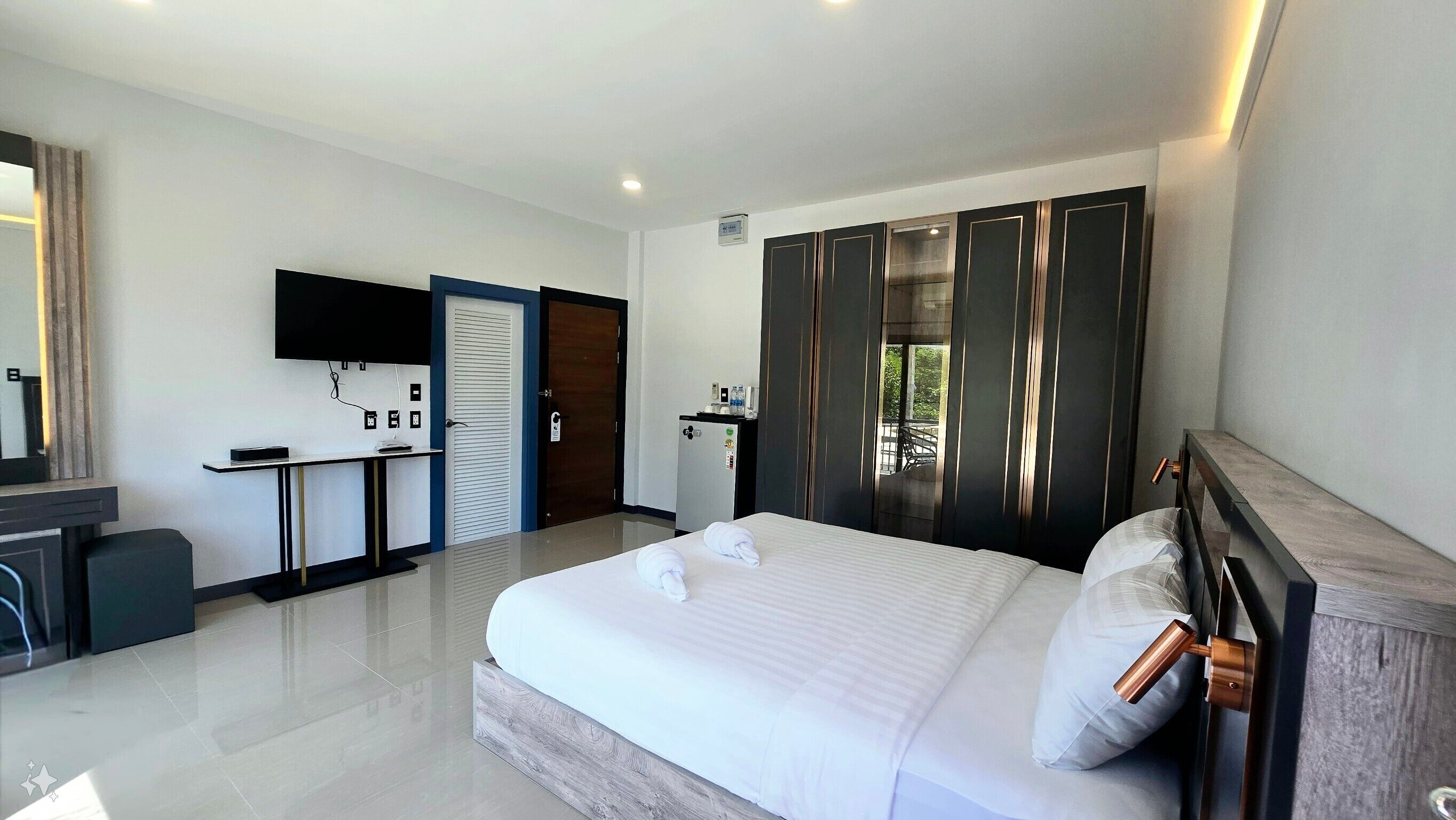 A hotel room with a large bed, a desk, a wardrobe, and a TV mounted on the wall.
