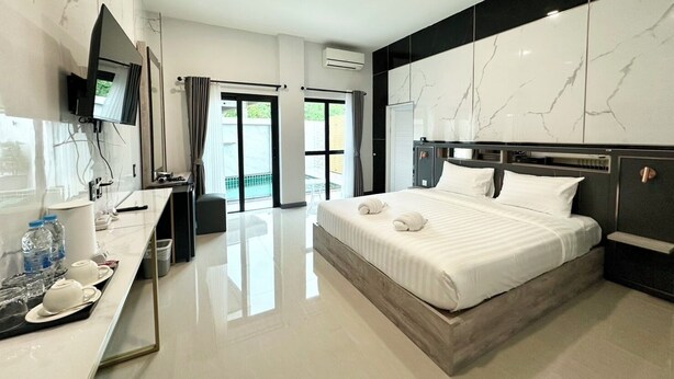 A modern hotel room with a large bed, a flat-screen TV, a desk with toiletries, and a balcony with a view. - Smile Boutique at Saiyuan (Rawai)