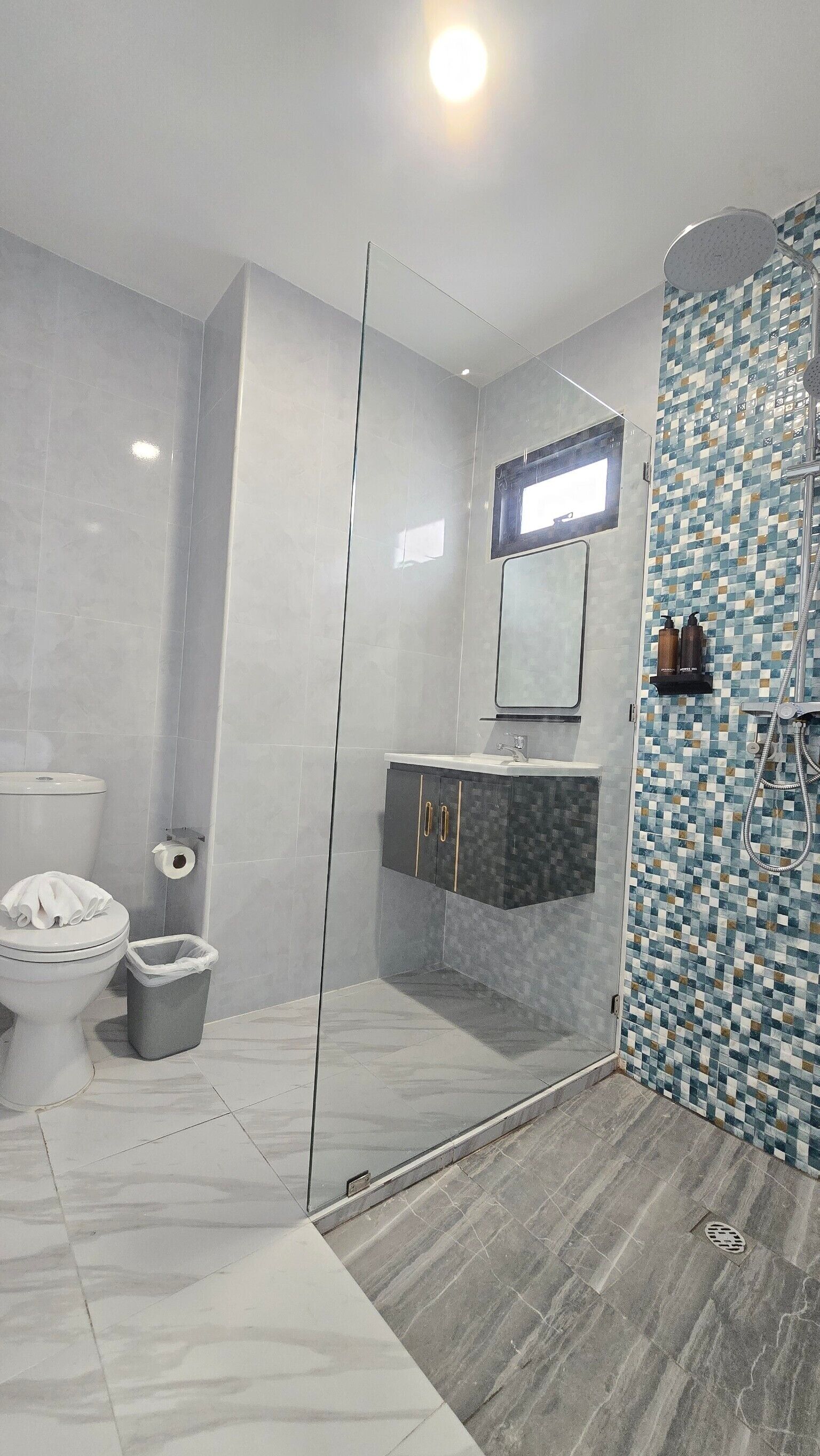 Ein modernes Badezimmer mit Duschkabine aus Glas, Toilette, Waschbecken mit Spiegel und gefliesten Duschwänden.