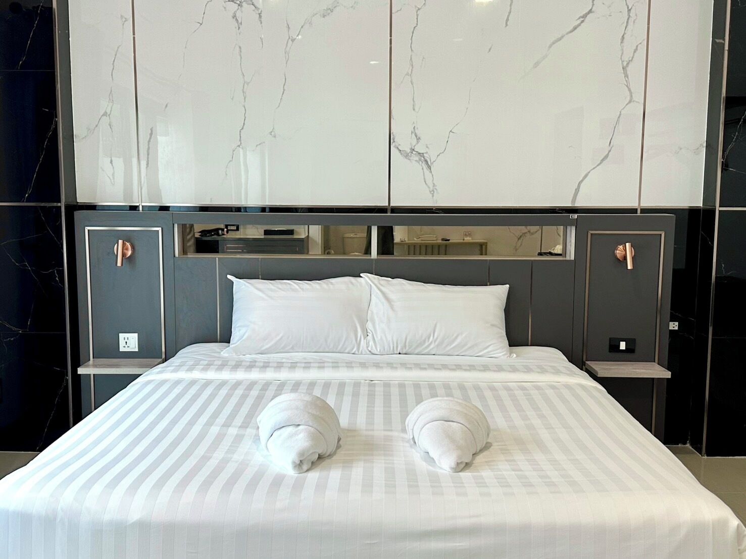 Ein Hotelzimmer mit einem großen Bett, zwei Nachttischen, einer Marmorwand und einem modernen Design.