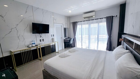 A hotel room with a large bed, a TV mounted on the wall, a desk with a chair, and a window with curtains.
