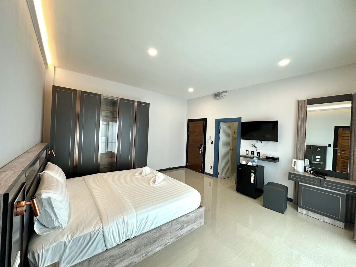 A modern hotel room with a large bed, a TV, a minibar, and a wardrobe.