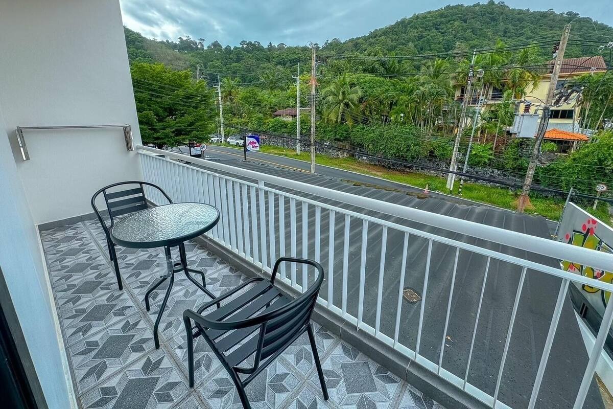Un balcon avec deux chaises et une table, donnant sur une route où la vitesse maximale autorisée est de 50 km/h, et sur une colline verdoyante en arrière-plan.