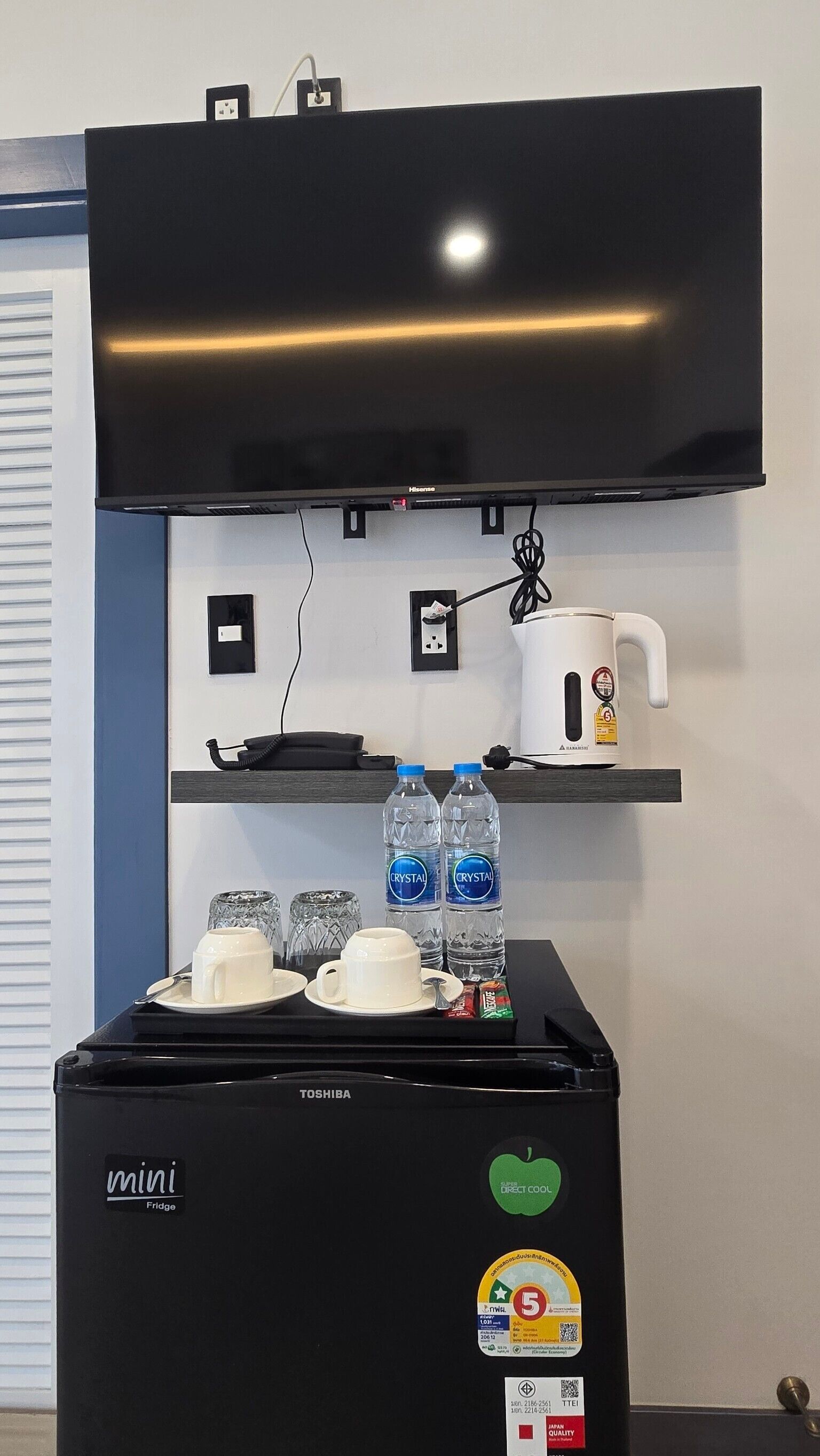 A mini fridge with a Toshiba logo, a coffee maker, two Crystal water bottles, and a mini fridge with a Direct Cool logo.