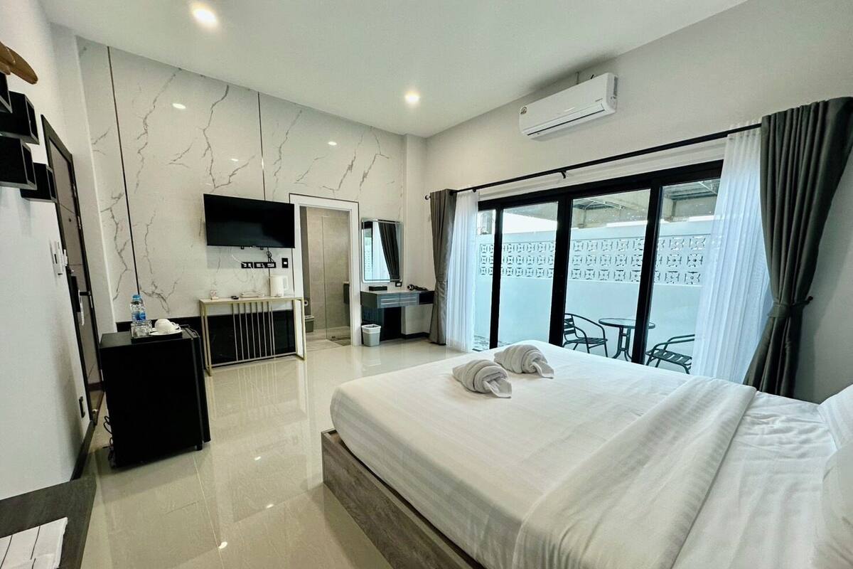 Une chambre d’hôtel moderne dotée d’un grand lit, d’un bureau avec un téléviseur à écran plat, d’un minibar et d’un balcon avec vue.