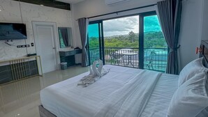 A modern hotel room with a large bed, a TV mounted on the wall, a balcony with a view of the greenery, and a small table and chair set. - Smile Boutique at Saiyuan (Rawai)