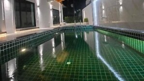 A nighttime view of a swimming pool with tiled flooring and a surrounding building with balconies and lighting. - Smile Boutique at Saiyuan (Rawai)