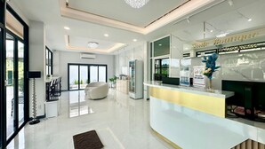 A modern reception area with a white reception desk, a chandelier, and a large window offering a view of the outdoors. - Smile Boutique at Saiyuan (Rawai)