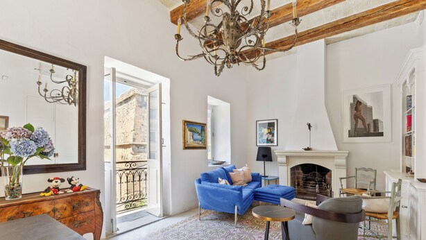 Una sala de estar con un sofá azul, chimenea, candelabro y vistas a través de un ventanal.
