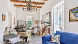 Una sala de estar con un sofá azul, piso estampado, una araña y un comedor con sillas y una mesa.