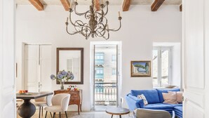 Un salón amplio con un sofá azul, una zona de comedor con una mesa y sillas, y una lámpara de araña.
