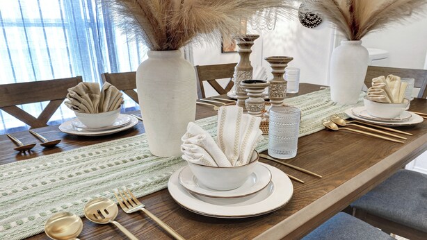 Una mesa de comedor con platos blancos, cubiertos dorados y un mantel tejido.