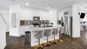 Una cocina moderna con armarios blancos, un refrigerador de acero inoxidable y una encimera de granito.