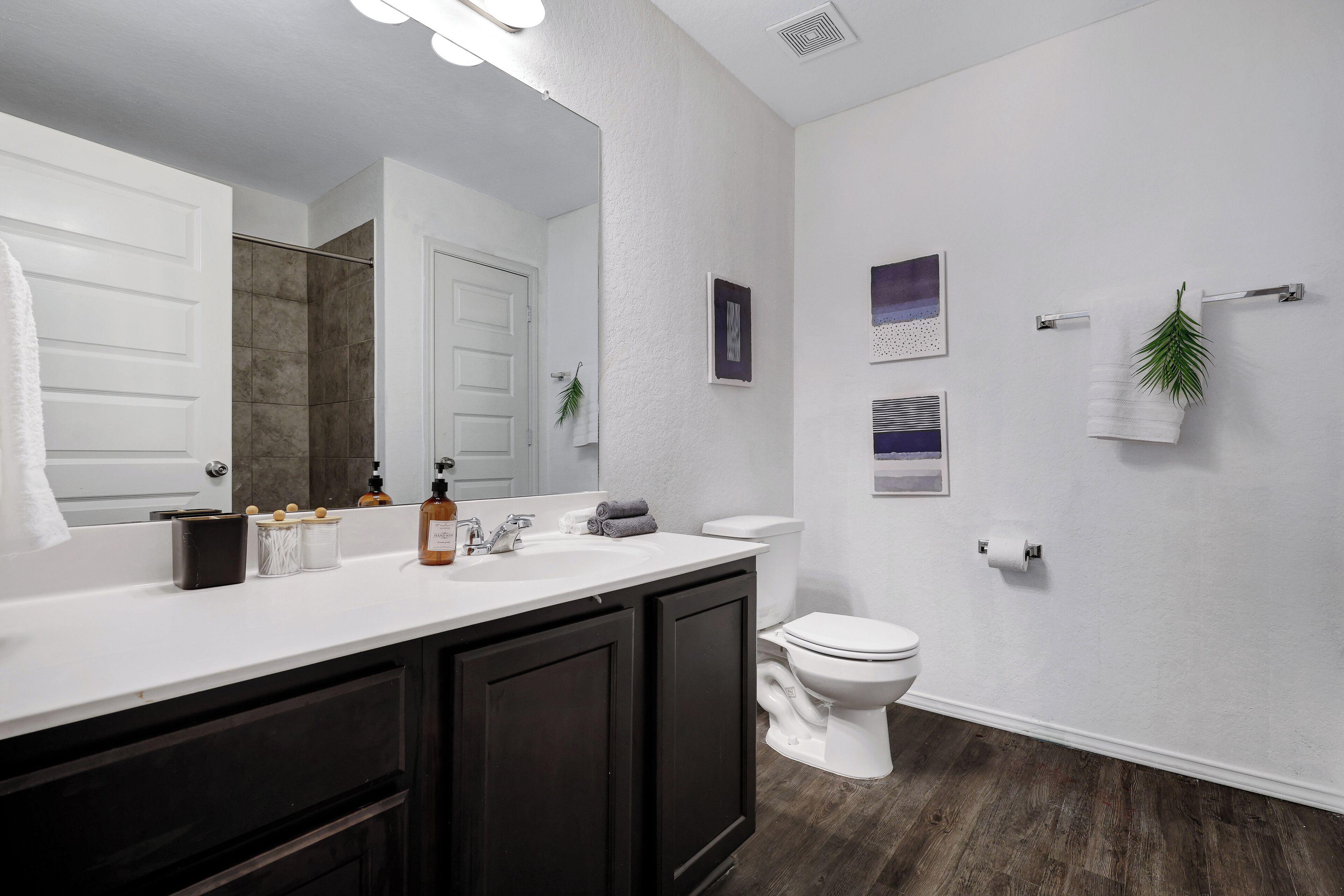 Un baño moderno con tocador blanco, muebles de color oscuro, inodoro blanco y zona de ducha.