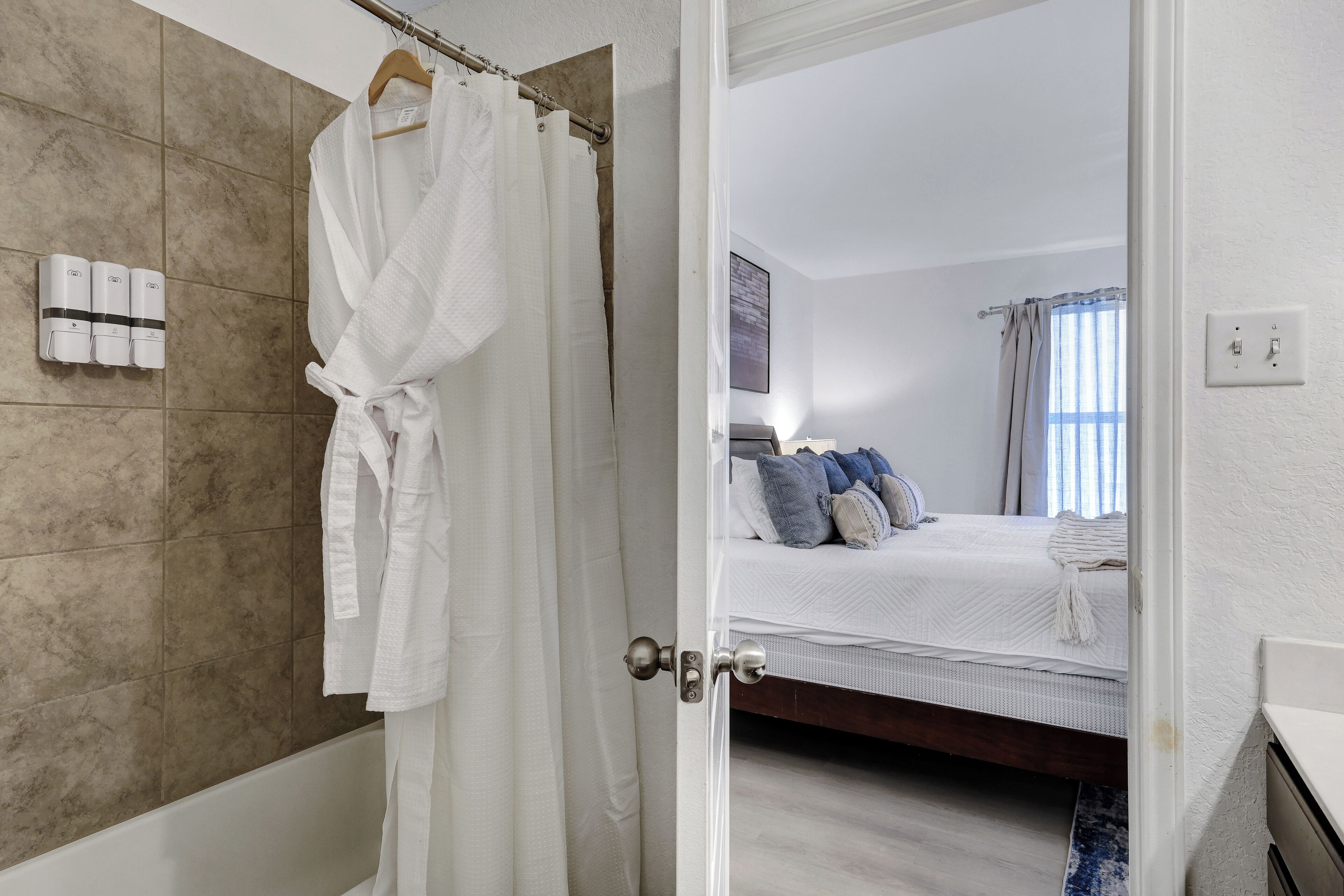 Habitaci ón de hotel con bañera, cama con almohadas y una bata blanca colgada en un perchero.