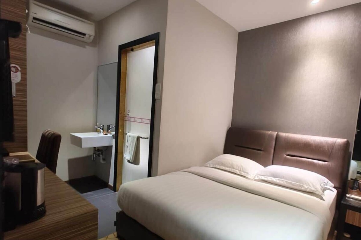 Een hotelkamer met een bed, een bureau, een spiegel, een wastafel en een airconditioning.