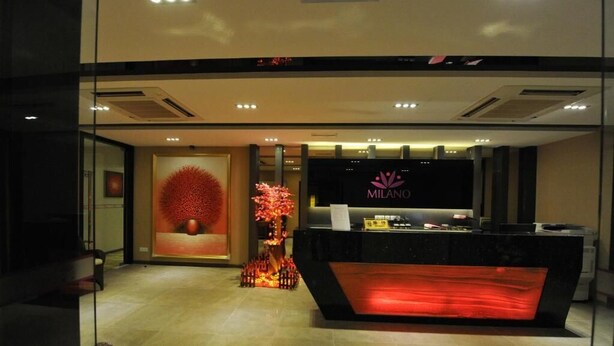 A reception area with a modern design, featuring a reception desk, a large screen displaying the hotel name, and decorative elements including a red spherical sculpture and a tall red tree-like structure. - MILANO HOTEL (Kluang)