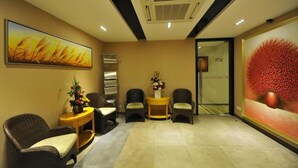 A reception area with wicker chairs, a small table with a vase of flowers, and a painting of wheat on the wall. - MILANO HOTEL (Kluang)