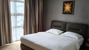 A hotel room with a large bed, a headboard, a window with curtains, and a wall-mounted picture. - MILANO HOTEL (Kluang)