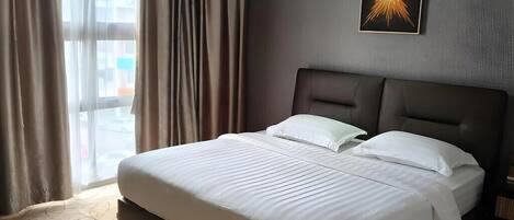 A hotel room with a large bed, a headboard, a window with curtains, and a wall-mounted picture.
