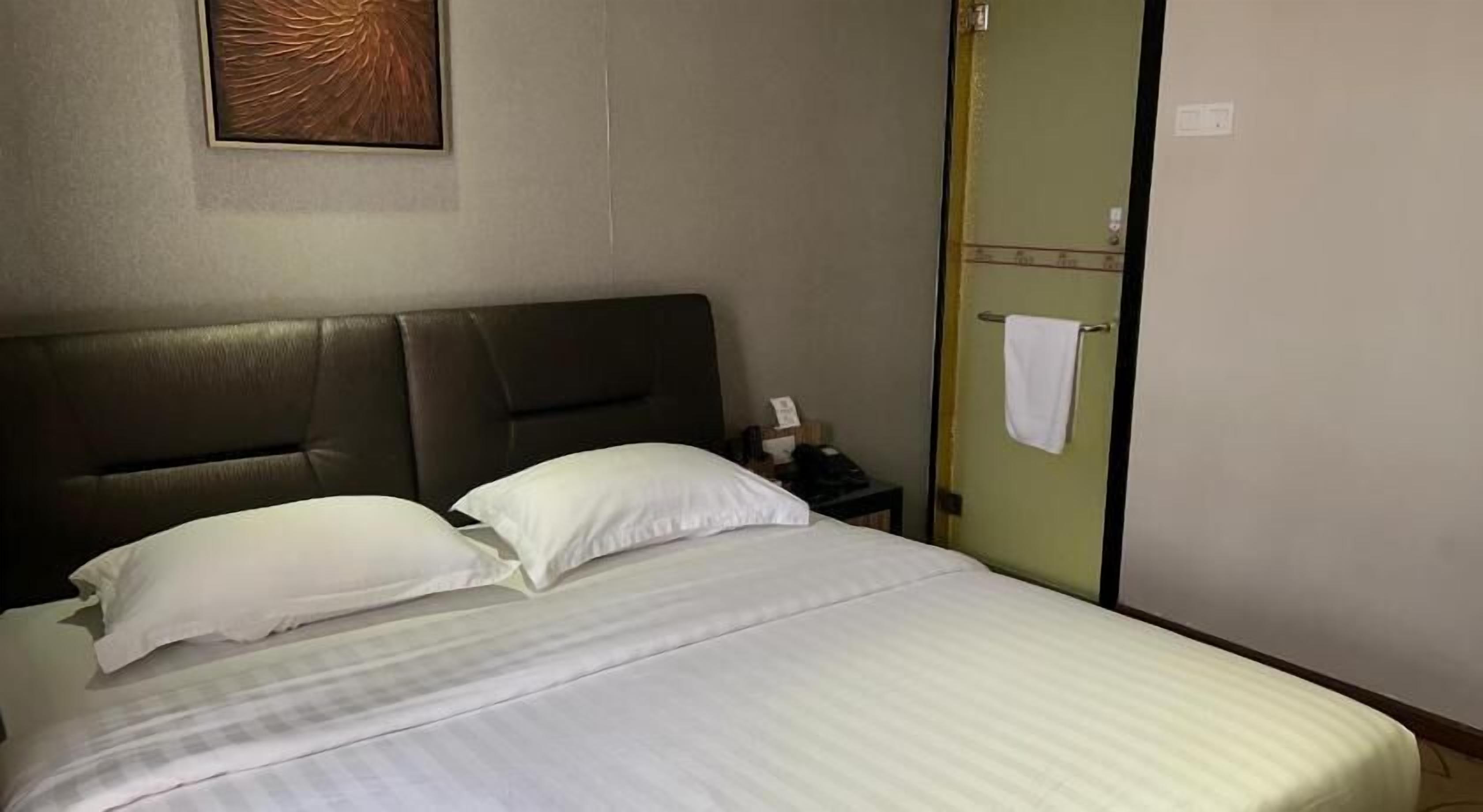 Una habitación de hotel con cama, almohadas, una mesita de noche y un perchero para toallas.