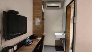 A hotel room with a flat-screen TV mounted on the wall, a wooden bench with a tray of toiletries, a white sink with a mirror, and an air conditioning unit above the sink. - MILANO HOTEL (Kluang)